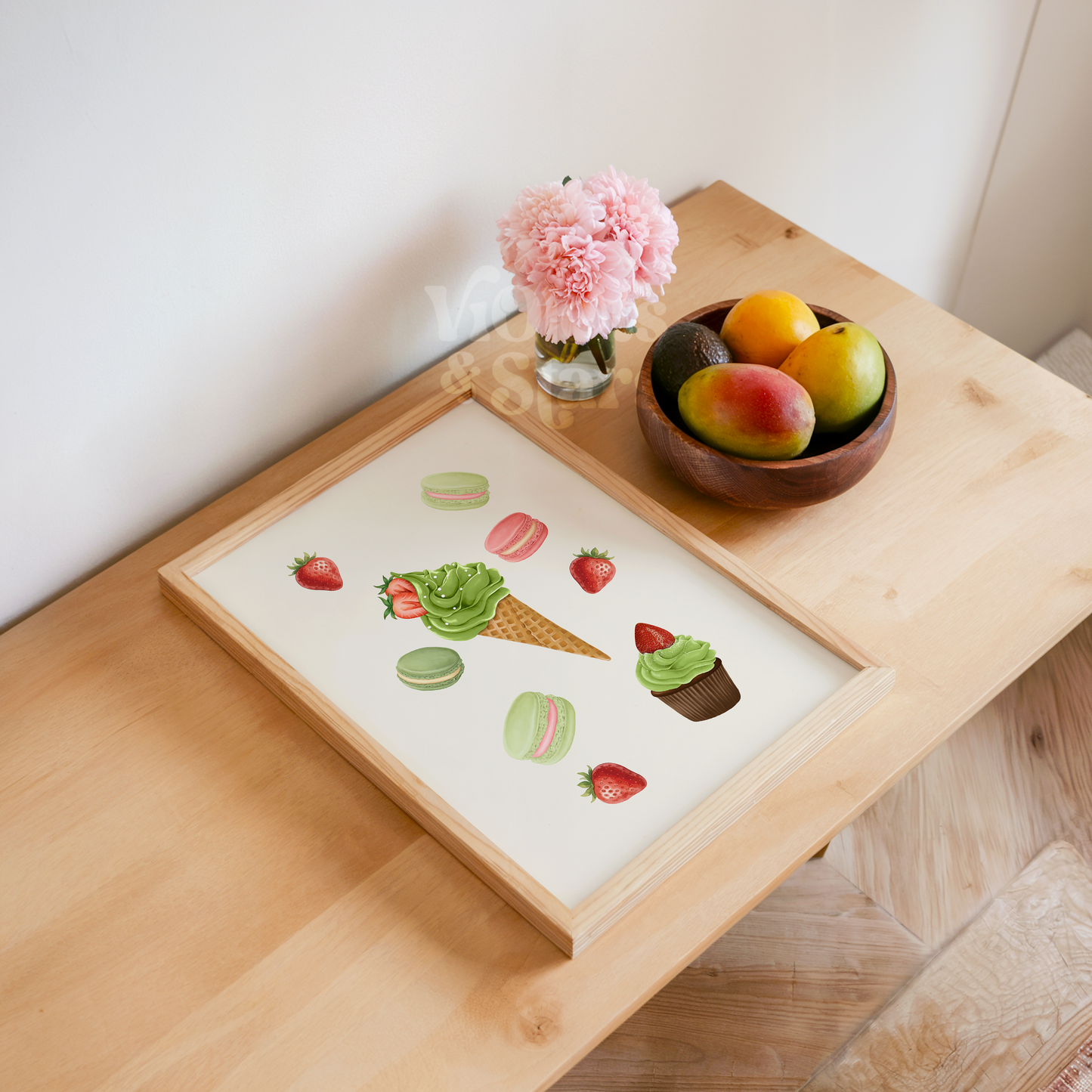 Wooden tray with a dessert illustration, bowl of fruit, and pink flowers on a wooden surface.